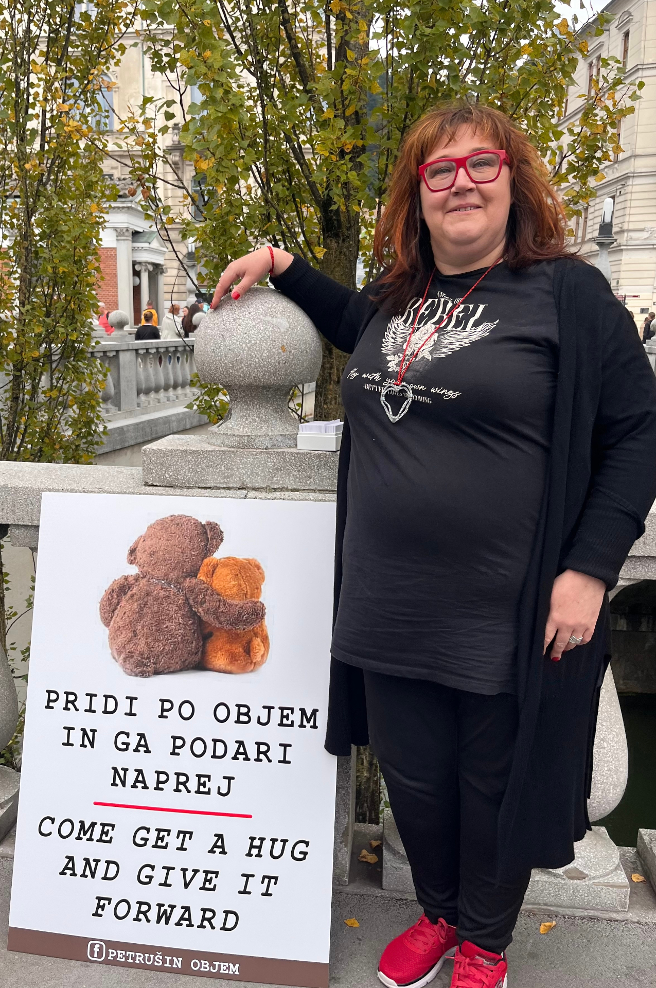 Petruša s tablo 'Pridi po objem in ga podari naprej' na Tromostovju
